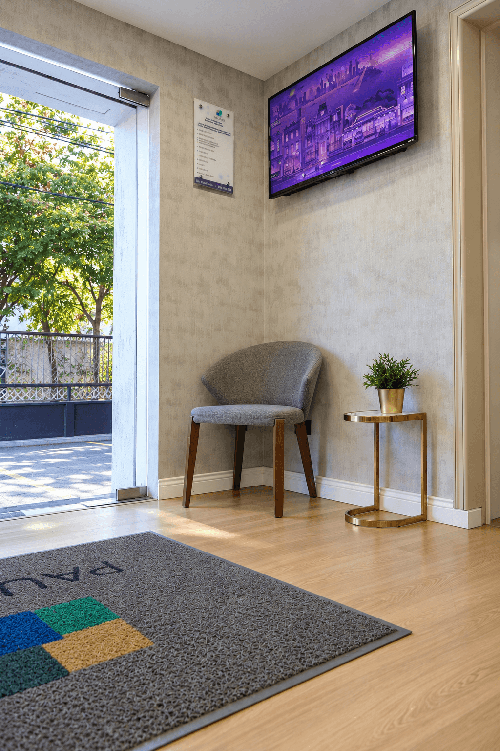 Zona de espera junto a la puerta de entrada, con una silla, una mesa y una pantalla.