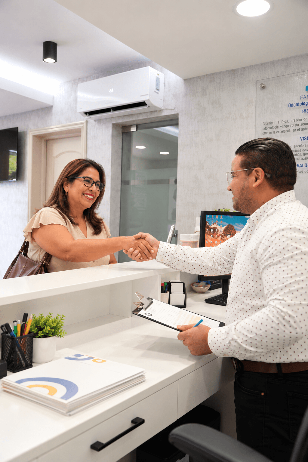 Una paciente y un integrante del equipo se saludan en el mostrador de recepción de PAUDENT.